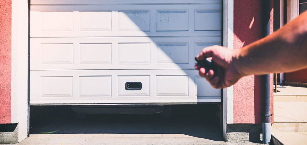 Persons hand clicking garage door opener opening a garage door