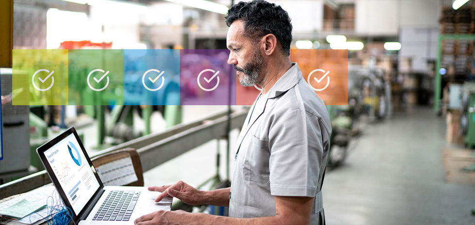 A man at a computer in a warehouse with multicolored checkmarks behind him