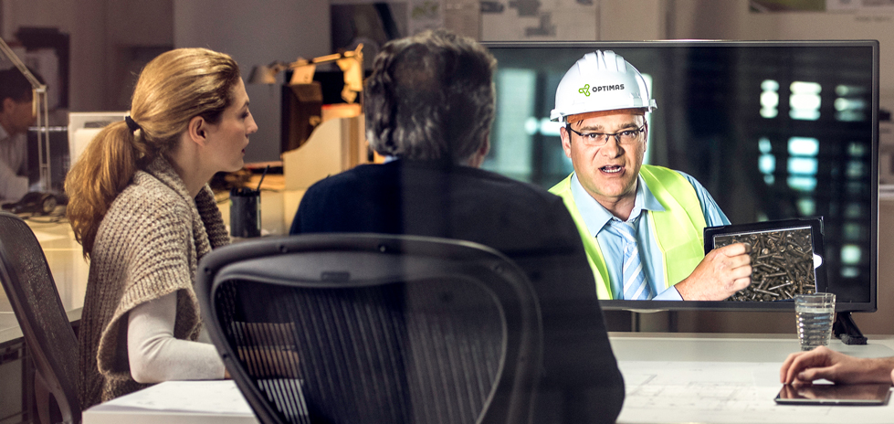 Three people watching a video on a TV screen with a man in a white hardhat with the Optimas logo on it