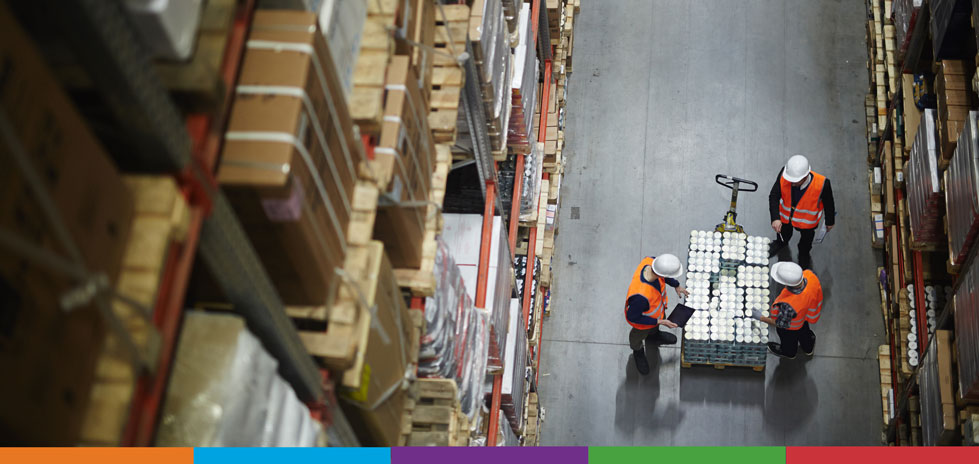 Three men in hardhats in a warehouse talking over a pallet