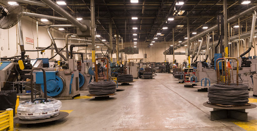 倉庫の床にファスナーのスプールとファスナー切断機が並んでいるオプティマス ファスナー製造施設
