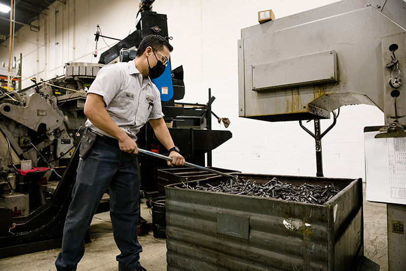Mann hält einen langen Metallstab über einen Behälter mit geschnittenen Verbindungselementen in der Produktionsanlage von Optimas Wood Dale.